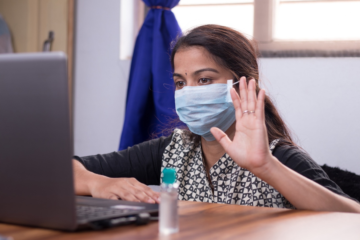 Woman with mask waving to computer screen